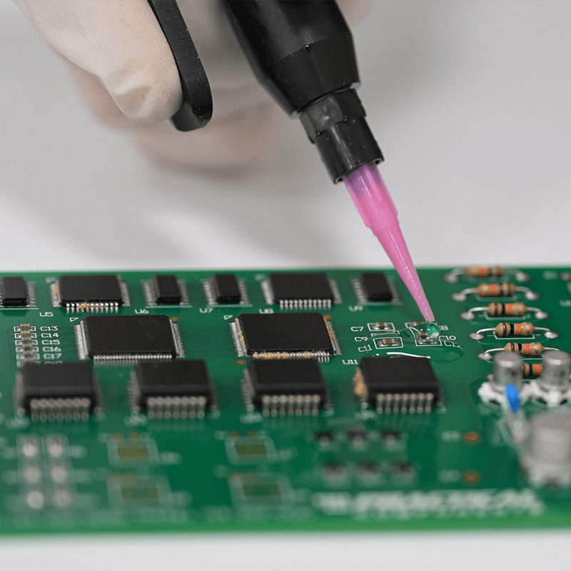 Close-up of a handheld valve applying encapsulation material to components on a circuit board