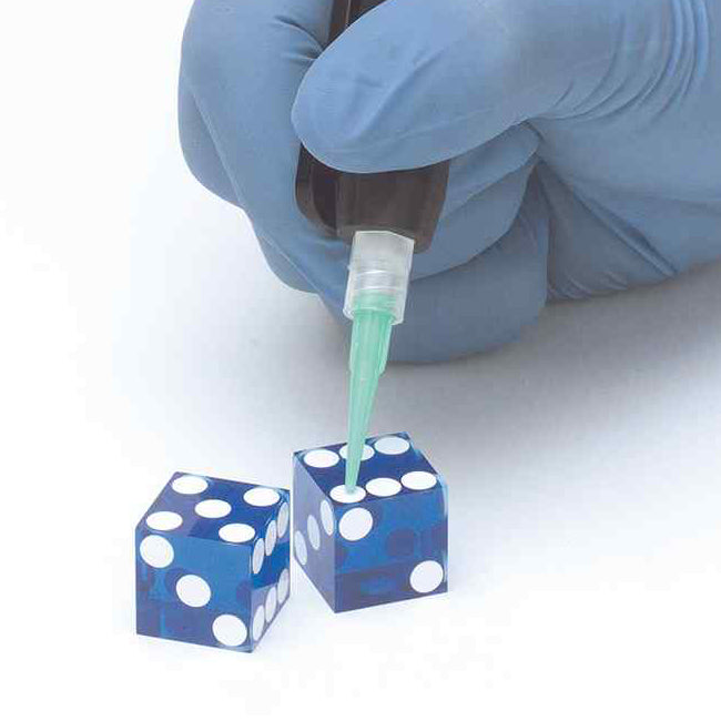 Close-up of a handheld diaphragm dispensing valve applying material onto small dice components with precision.